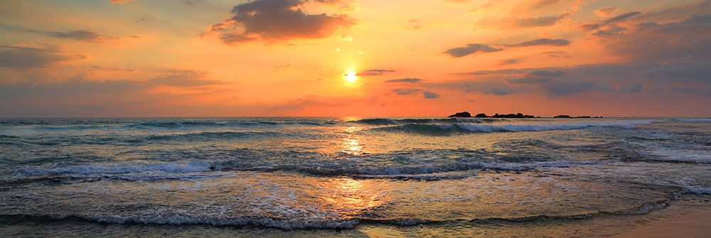 Sun setting on horizon of sandy beach with gentle waves